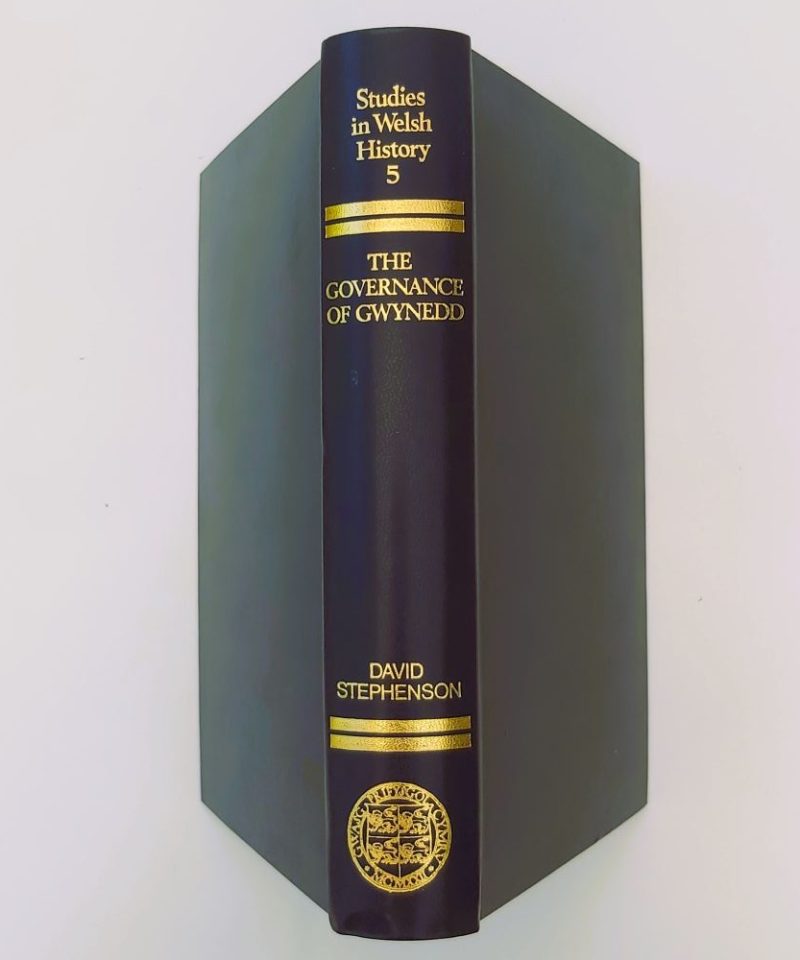 Governance of Gwynedd Close-up view of the spine of the book bound in dark blue cloth, showcasing vibrant gilt-stamped lettering for the title, author, series number 5, and the University of Wales crest Stephenson (3)a