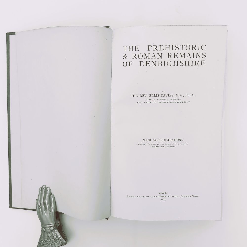 Prehistoric and Roman Remains of Denbighshire Davies (2)a Open title page of the 1929 book "The Prehistoric & Roman Remains of Denbighshire" by The Rev. Ellis Davies, printed by William Lewis in Cardiff, held open by a silver metal hand weight.