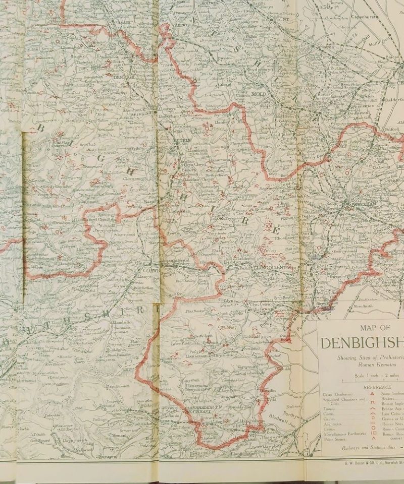 Prehistoric and Roman Remains of Denbighshire Davies (5)a : A large, detailed, multi-folding color map of Denbighshire by G.W. Bacon and Co., featuring a red border and specific symbol references for prehistoric caves, camps, and Roman roads.